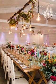 a long wooden table topped with lots of white chairs and tables covered in floral centerpieces