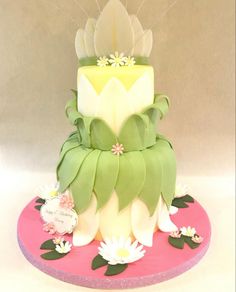 a three tiered cake with flowers and leaves on it's side, sitting on top of a pink plate