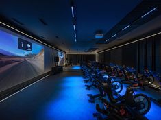 a large room with many bikes in it and blue lights on the ceiling, along with an interactive screen