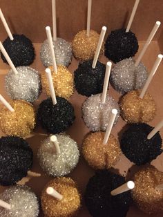 a box filled with cake pops covered in black, gold and white frosting