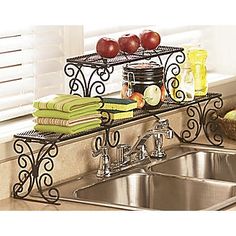 a kitchen sink sitting under a window next to a metal shelf filled with fruit and vegetables