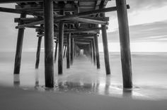 black and white photograph of the ocean under a pier