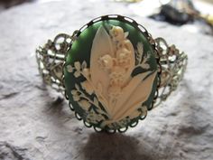 Beautiful lily of the valley cameo bracelet I have many other styles and cameo colors, please feel free to message me with the color you would like. I have many matching pieces, so please do browse for the complete look. The bracelet is adjustable, with pretty filigree. I will be glad to do special requests or matching locket, and/or brooch if you don't see it I can make it!! Please any questions feel free to ask Thanks so much for looking Lisa.... Cameo Bracelet, Brass Cuff Bracelet, Filigree Bracelet, Vertical Gardens, Cameo Jewelry, Urn Necklaces, Dope Jewelry, Cameo Brooch, Pin Pendant