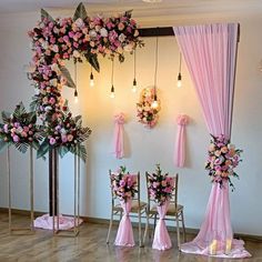 a room decorated with pink and white flowers on the wall, chairs covered in draping