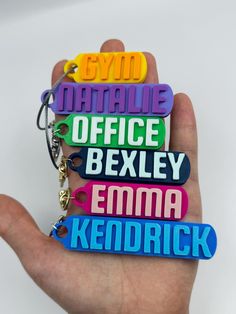 a hand holding three different colored keychains that say office bexley, emma kendrick, and natalie bexley