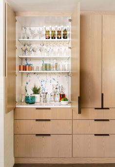 a kitchen with wooden cabinets and glassware on the counter top, in front of an open cabinet door