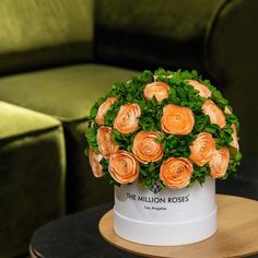 a white vase with orange flowers on a table in front of a green chair and couch