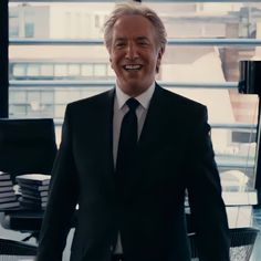 an older man in a suit and tie smiles at the camera while standing in front of a window