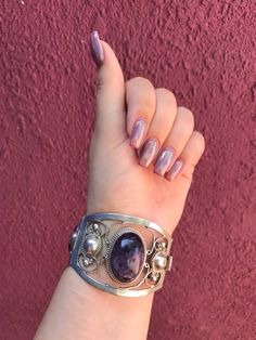 This stunning sterling silver cuff features three oval-shaped amethyst stones and an easy-to-use slide-in clasp. Handcrafted in Mexico, the intricate designs of silver swirls surround the amethysts in an ethereal way. The back of the clasp reads Sterling Mexico, as pictured. This high quality piece would be the perfect finish to an elaborate look for a festival, dinner, or cocktail party. Get ready to be showered in compliments for your stunning silver and purple amethyst bracelet! Amethyst is a Elegant Purple Gemstone Cuff Bracelet, Silver Amethyst Gemstone Cuff Bracelet, Handmade Silver Amethyst Cuff Bracelet, Silver Oval Cuff Bracelet With Polished Finish, Purple Amethyst Bohemian Cuff Bracelet, Elegant Silver Amethyst Cuff Bracelet, Amethyst Stones, Chunky Bracelets, Amethyst Bracelet