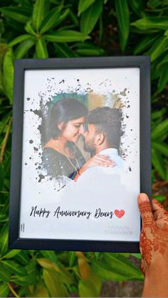 a person holding up a framed photo with the words happy anniversary