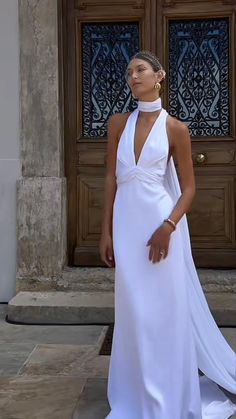 a woman standing in front of a door wearing a white dress with a halter neck