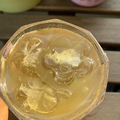 a person holding up a glass filled with ice and lemonade on top of a wooden table