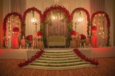 a decorated stage with red flowers and greenery on the steps leading up to a couch