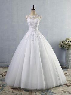 a white wedding dress on a mannequin in front of a vase with flowers