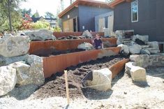 a woman sitting on top of a pile of rocks in front of a house next to a garden