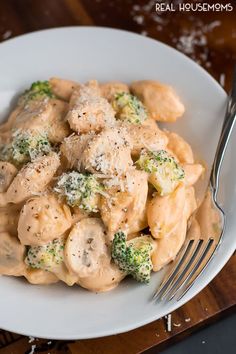 a white plate topped with pasta and broccoli covered in sauce next to a fork