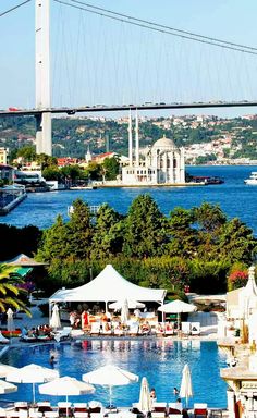 an outdoor swimming pool with umbrellas and tables in front of the bridge over water