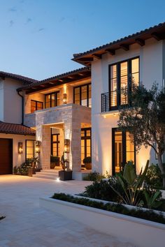 a large white house with lots of windows and plants in the front yard at night