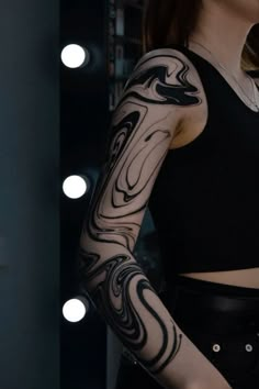 a woman with black and white tattoos on her arm is standing in front of a mirror