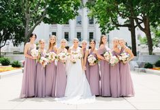 a group of women standing next to each other in front of a building with trees