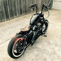 a black motorcycle parked in front of a wooden fence with its lights on and the seat up