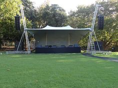 an outdoor stage set up in the middle of a grassy area with trees behind it