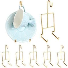 a cup and saucer are hanging from hooks on a white background with gold clips