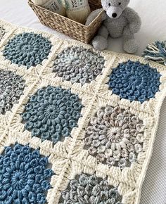 a crocheted afghan with a teddy bear next to it and a basket full of yarn