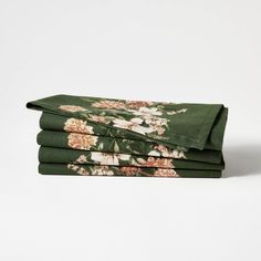 four folded sheets with flowers on them in dark green and pink colors, sitting on top of each other