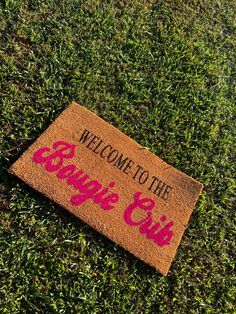 a welcome to the game girl door mat on grass with pink writing that says welcome to the game girl