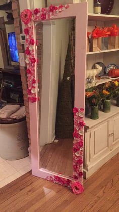 a pink mirror sitting on top of a wooden floor next to a shelf filled with flowers