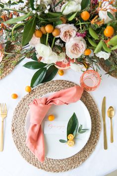 a place setting with oranges, flowers and greenery