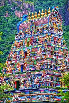 an elaborately decorated hindu temple with mountains in the backgrouds and trees around it