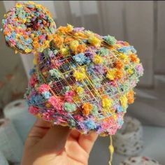 a person holding up a multicolored object made from yarn and crochet