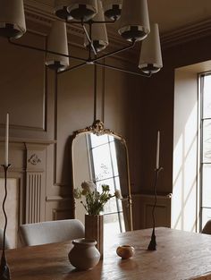 a dining room table with a mirror and vase on it, in front of two windows