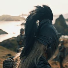 a man with long white hair wearing a helmet on top of a hill next to the ocean