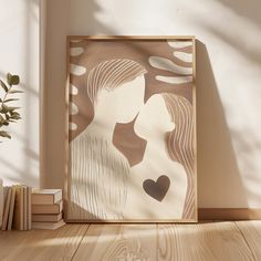 a framed art piece on a wooden floor next to books and a potted plant