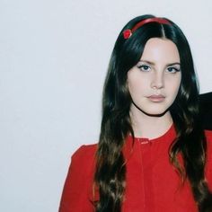 a woman with long black hair wearing a red shirt and headband standing in front of a white wall