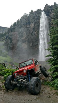 a red jeep is parked in front of a waterfall