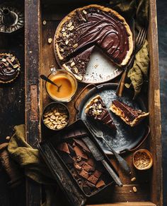 an overhead view of chocolate pies and other desserts on a wooden tray with spoons