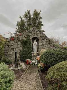 a statue in the middle of a garden with rocks and plants around it, surrounded by shrubbery