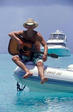 a man sitting on the back of a boat while holding a guitar