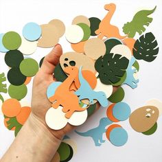 a hand is holding some paper cutouts in the shape of dinosaurs and other animals