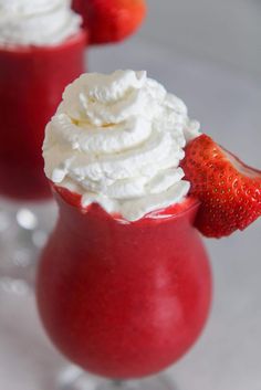 two glasses filled with red drinks and topped with whipped cream, strawberries on the rim