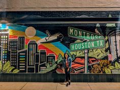 a woman standing in front of a mural on the side of a building with street signs