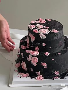 a black cake with pink flowers on it being held by a person's hand