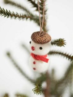 a small snowman ornament hanging from a pine tree with needles on it