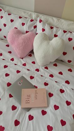 two heart shaped pillows sitting on top of a bed next to an open laptop computer