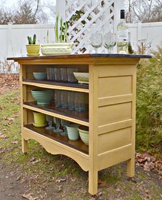 an old dresser is turned into a potting bench with dishes on it and glassware in the bottom drawer