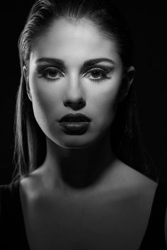 black and white photo of a woman with makeup on her face, looking at the camera